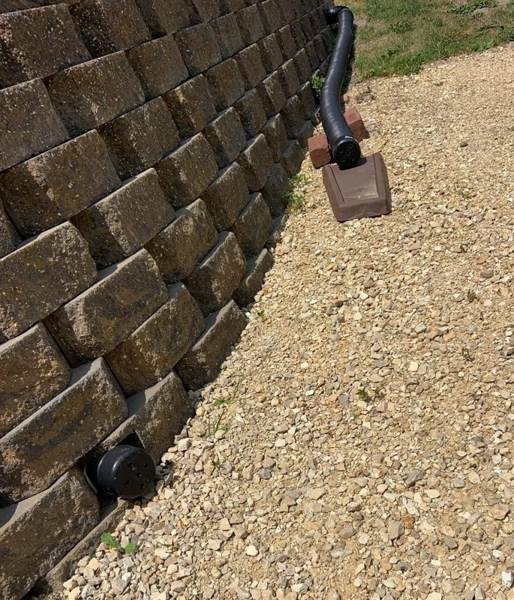 A completed gravel-covered drain beside a retaining wall. The buried collection pipe is not visible.